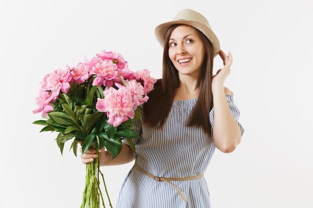 青いドレス、白い背景で隔離の美しいピンクの牡丹の花の花束を保持している帽子の若い優しい女性。聖バレンタインの日、国際女性の日の休日の概念。広告エリア。