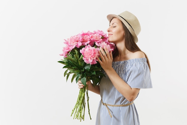 Giovane donna tenera in abito blu, cappello che tiene, sniffing bouquet di fiori di peonie rosa isolati su sfondo bianco. san valentino, concetto di vacanza per la giornata internazionale della donna. zona pubblicità.