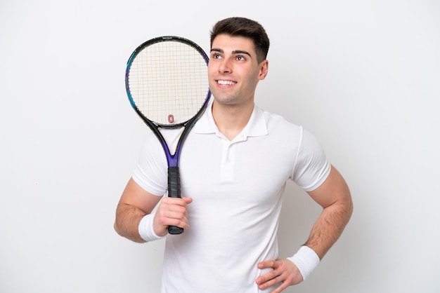 흰색 배경에 고립 된 젊은 테니스 선수 남자 엉덩이에 팔을 포즈 하 고 웃 고
