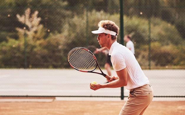 Young tennis player in sportive clothes is on the court outdoors.