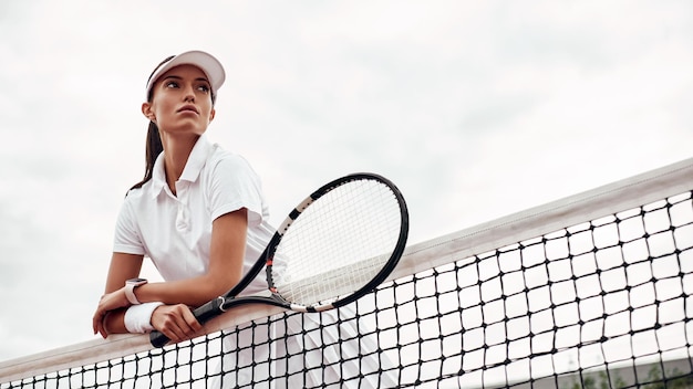 Молодой теннисист стоит на корте и держит ракетку