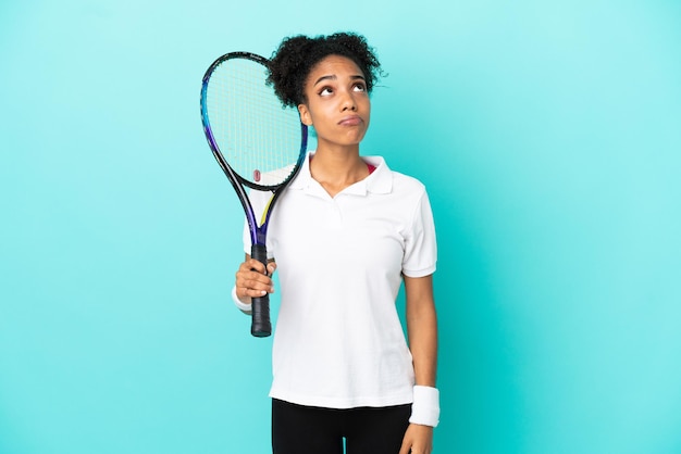 Young tennis player woman isolated on blue background and looking up