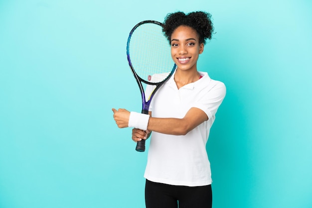 Young tennis player woman isolated on blue background pointing back