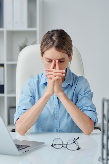 Young tense businesswoman keeping her hands by face while trying to concentrate on work and thinking about new strategies in office