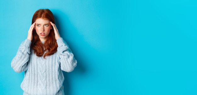 Young tensed redhead college girl trying to think rubbing temples and looking up thinking standing o