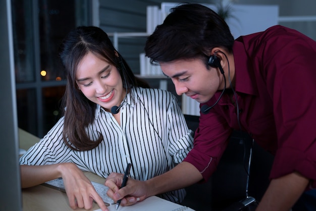 Young Thai Asian customer services care operators working night shift in call center for helping assistance client in workplace at night time