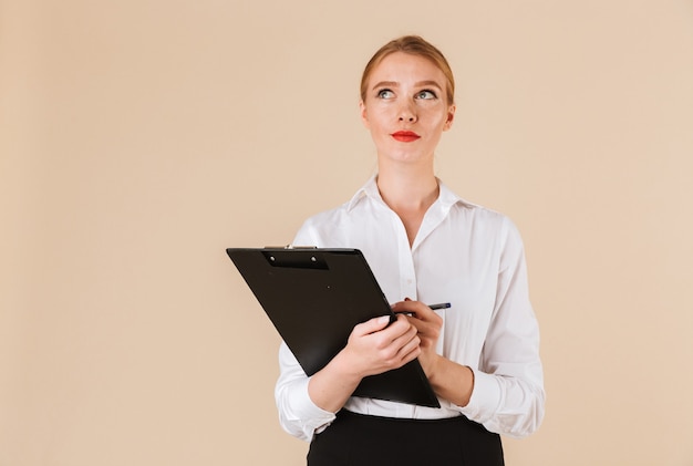 Young thinking business woman holding clipboard. Looking aside.