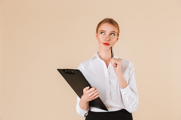 Young thinking business woman holding clipboard. Looking aside.