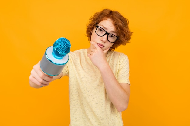 Young thinking red-haired guy in a shirt and glasses on a yellow background
