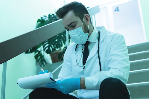 Young thoughtful doctor making last notes in the report after long shift