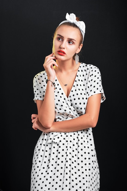 Young thoughtful girl with pin-up make-up and hairstyle posing in studio.