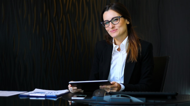 Young thoughtful secretary using a digital tablet at her desk smiling