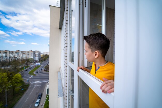 Young thoughtful teenage boy is standing on a balcony and thinking about life.