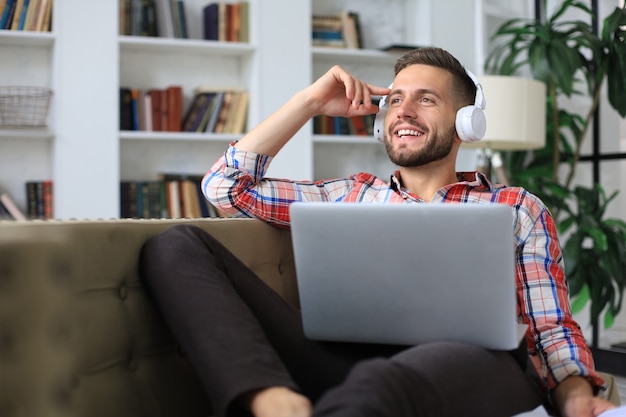 Giovane libero professionista stanco in abbigliamento casual seduto sul divano davanti al computer portatile.