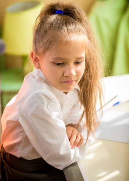 Young tired girl in school uniform sitting at desk with homework