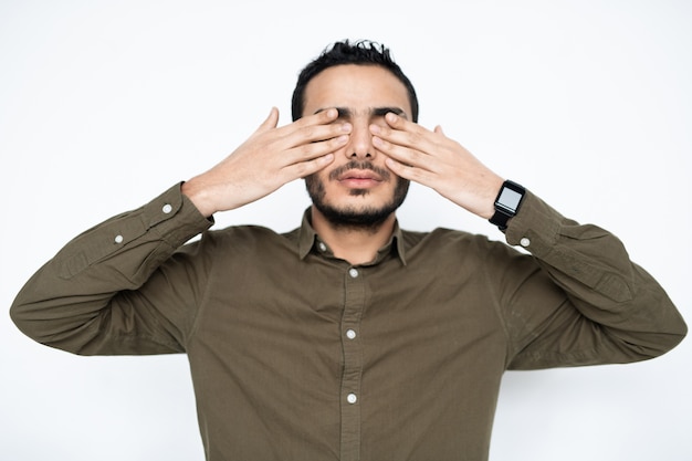 Giovane uomo stanco in camicia che copre gli occhi con le mani in pausa tra il lavoro mentre ci si rilassa in isolamento