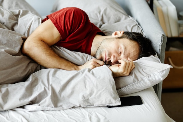 Young tired man sleeping in his bed under blanket in the bedroom