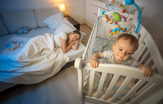 Young tired mother got asleep next to baby's crib at night