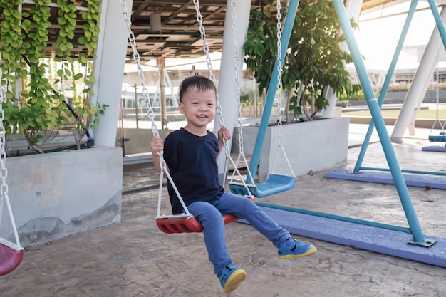 young toddler boy child having fun swinging at children playground