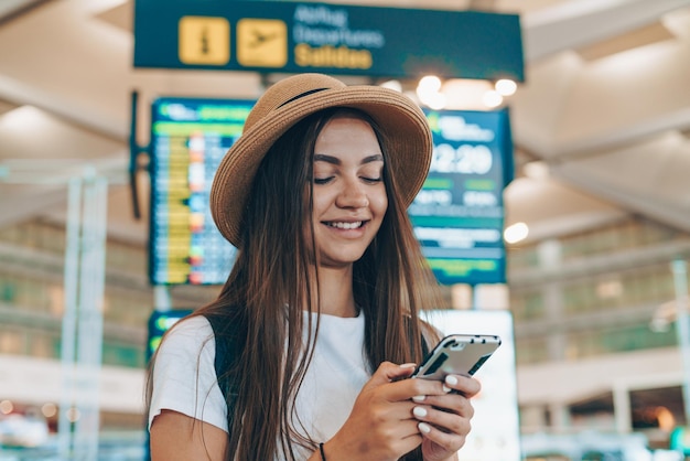 Young tourist at the airport stands on the background of the scoreboard and writes sms by phone