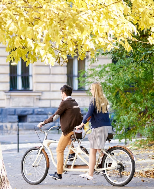 若い観光客カップル、ハンサムな男、街の通りに沿ってタンデム自転車に乗ってかなり金髪の女性。