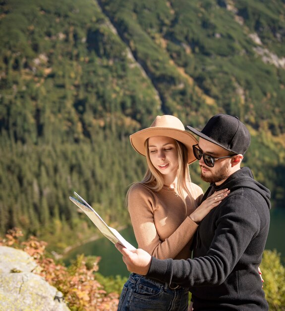 Young tourist couple, man and woman, on hiking path in mountains, holding  map and finding way in nature on sunny day