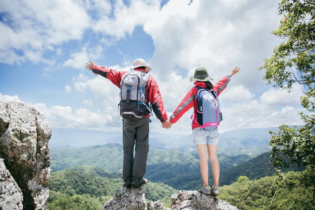 Young tourist couple watching spectacular mountain scenery in high mountains man and woman hiker on top rock A couple of travelers in love People greet the dawn Lovers travel Copy space