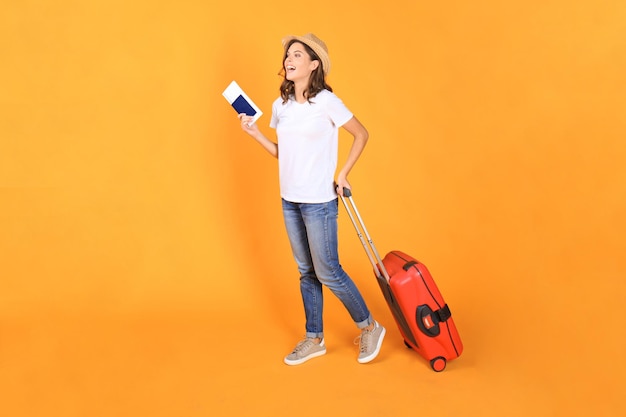 Giovane ragazza turistica in abiti casual estivi, con valigia rossa, passaporto, biglietti isolati su sfondo beige