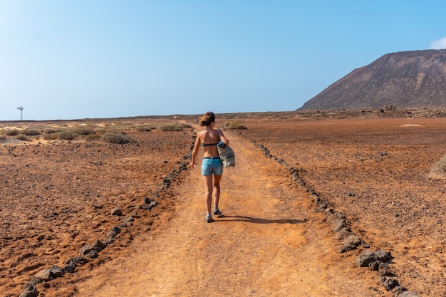 Una giovane ragazza turistica percorrendo i sentieri di isla de lobos, lungo la costa nord dell'isola di fuerteventura, isole canarie. spagna