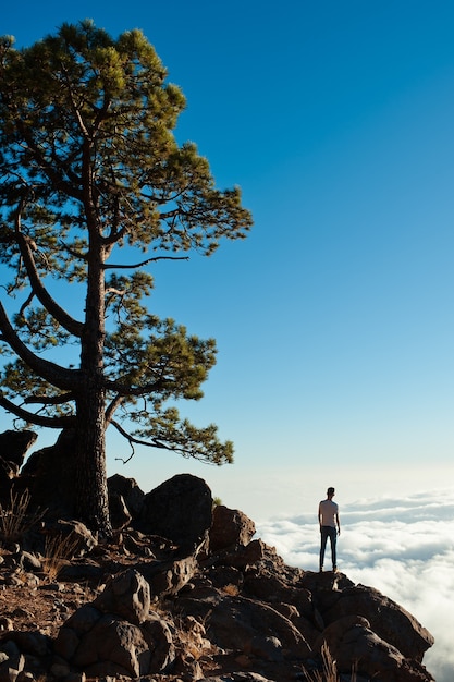 Young tourist man on top of mountains admires sky and clouds