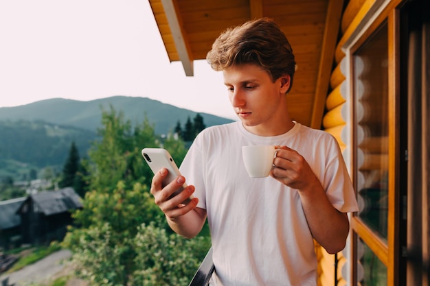 A young tourist man with a cup of coffee in his hands spends time on the balcony of the apartment