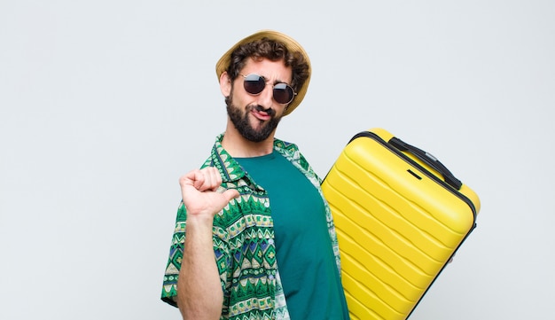 Young tourist man with a suit case against white wall. travel concept