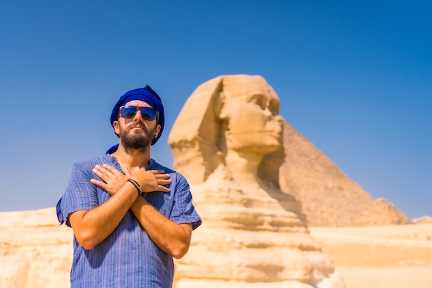 기자 대 스핑크스 근처에서 젊은 관광객이 기자의 미라 마이드가있는 곳에서 파란색과 파란색 터번을 입고 있습니다. 카이로, 이집트