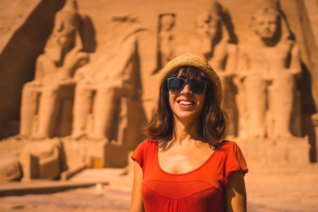 A young tourist in a red dress smiling at the Abu Simbel Temple in southern Egypt in Nubia.