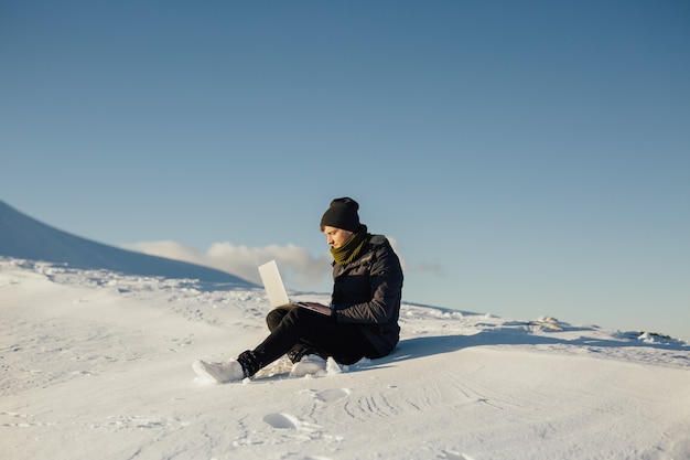 Young tourist using laptop on snowy mountain.