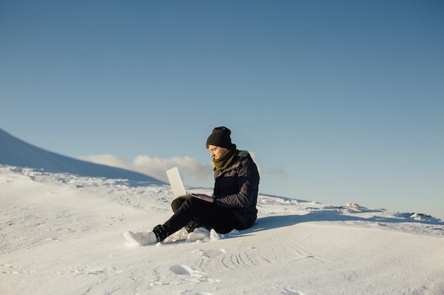 Giovane turista utilizzando laptop sulla montagna innevata.