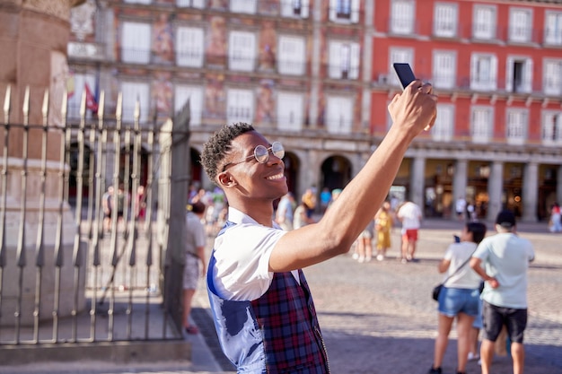 Молодой турист посещает площадь мэра в Мадриде, делая селфи со своим смартфоном