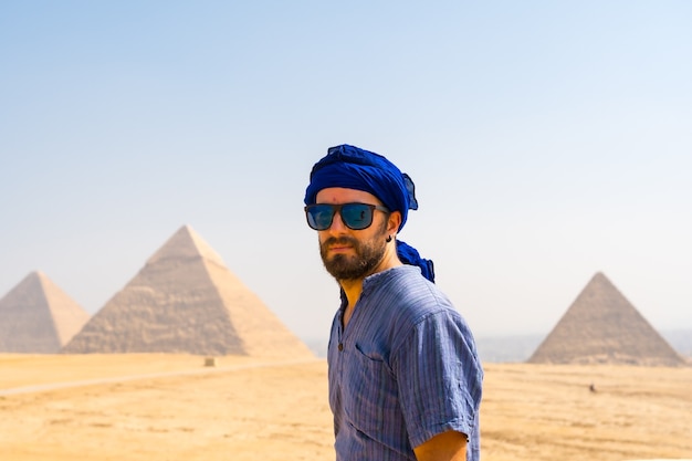 Un giovane turista che indossa un turbante blu e occhiali da sole mentre si gode le piramidi di giza, il più antico monumento funerario del mondo. nella città del cairo, in egitto