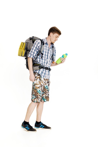 Young tourist with a backpack drinking water on a white background