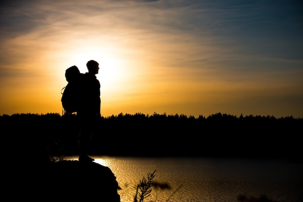 Young tourist with backpack standing on a rock and enjoying sunset