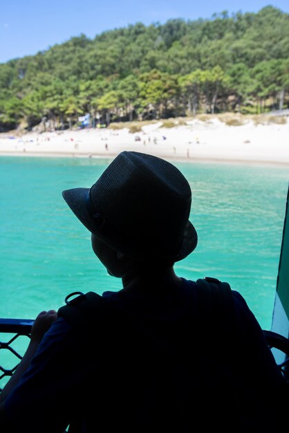 Photo a young tourist with a hat amazed on the side of a boat watching a white sand beach and turquoise waters