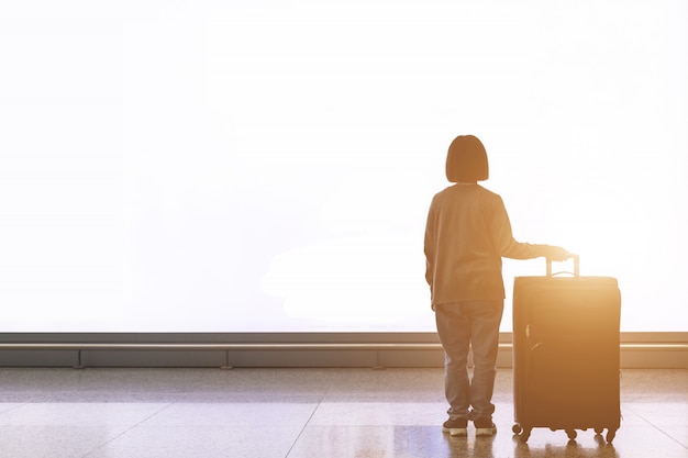 Young tourist with luggage standing in front of big white light billboard at the airport