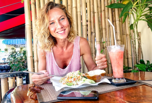 볶음밥을 먹고 태국 푸켓의 태국 레스토랑에서 과일 스무디를 마시는 젊은 관광 여성