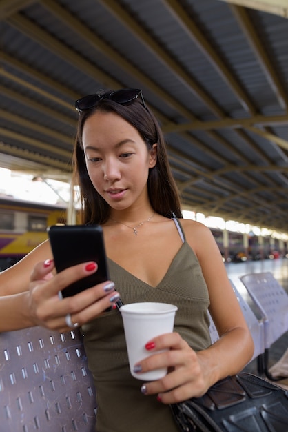 Молодая туристическая женщина пьет кофе и пользуется мобильным телефоном