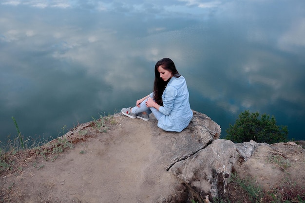 Young tourist woman is sitting on the top of the mounting and looking at a beautiful landscape. Hiking woman relaxing on the top of the cliff enjoying. attractive girl in denim clothes