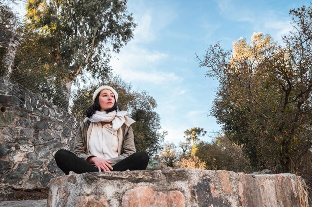 Молодая туристка сидит на большом камне и смотрит на пейзаж
