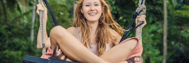 Young tourist woman on the swing in the jungle rainforest of a tropical bali island banner long