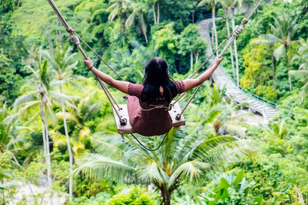 Young tourist woman swinging over the tropical rainforest at Bali island