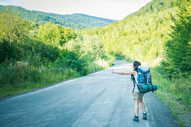 young touristic woman is hitchhiking in mountains with backpack