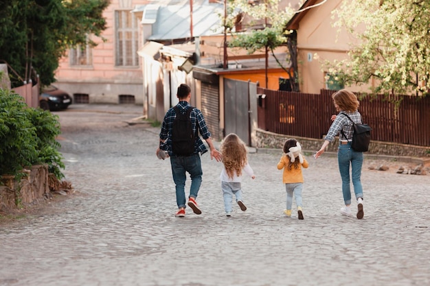 두 명의 사랑스러운 딸을 데리고 뒤에서 구시가지의 거리를 걷고 있는 젊은 관광객 가족